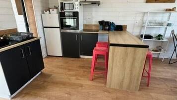 Une cuisine compacte dotée d’un îlot central, de meubles noirs et d’un tabouret rouge.