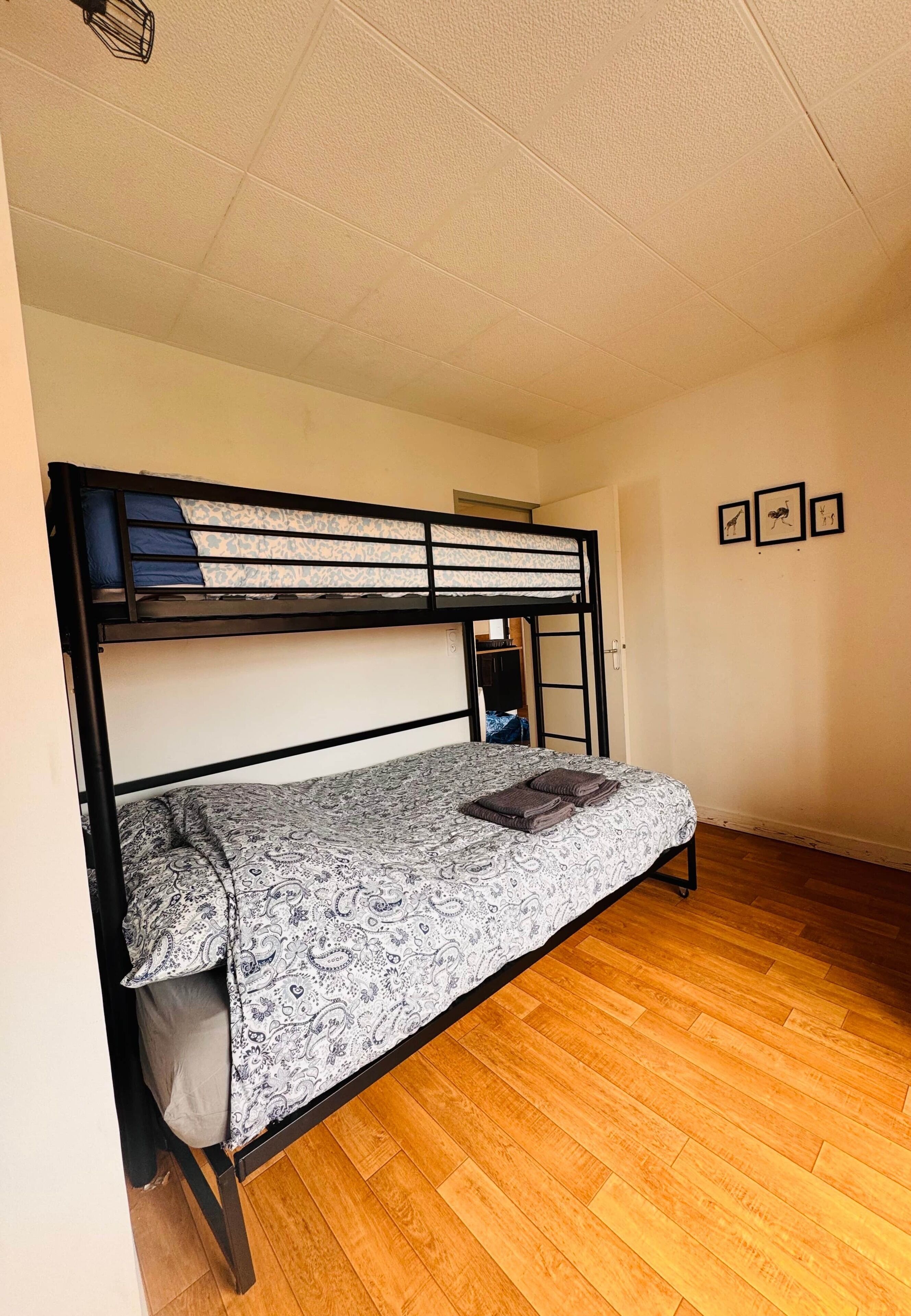 A bunk bed with a patterned bedspread and pillows, wooden flooring, and a ceiling with a light fixture.