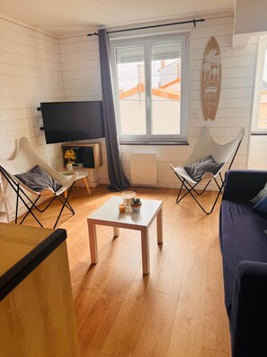 A living room with a TV, two chairs, a coffee table, and a surfboard on the wall.