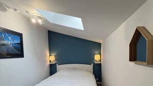 Ein Schlafzimmer mit Dachfenster, einem Bett, zwei Nachttischen mit Lampen und einem gerahmten Bild an der Wand.