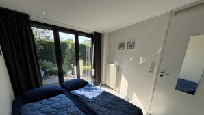 A bedroom with a large bed, a sliding glass door to a balcony, and a white door with a small picture. - Detached 4-person house with sauna, WLAN, fenced garden. (Brouwershaven)