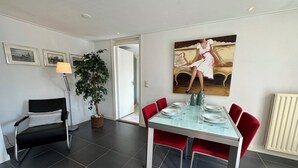 A dining area with a glass table, red chairs, and a painting on the wall. - Detached 4-person house with sauna, WLAN, fenced garden. (Brouwershaven)