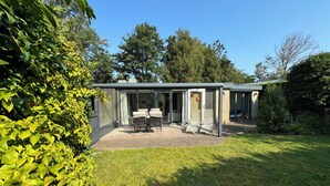 A modern house with a patio, two chairs, and a table. - Detached 4-person house with sauna, WLAN, fenced garden. (Brouwershaven)