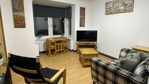 A living room with a TV, a sofa, a chair, and a small table.