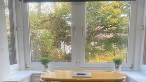 A dining area with a round table and two chairs, positioned near a window with a view of trees and buildings.