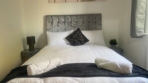 A neatly made bed with white and dark bedding, a grey headboard, and decorative pillows.