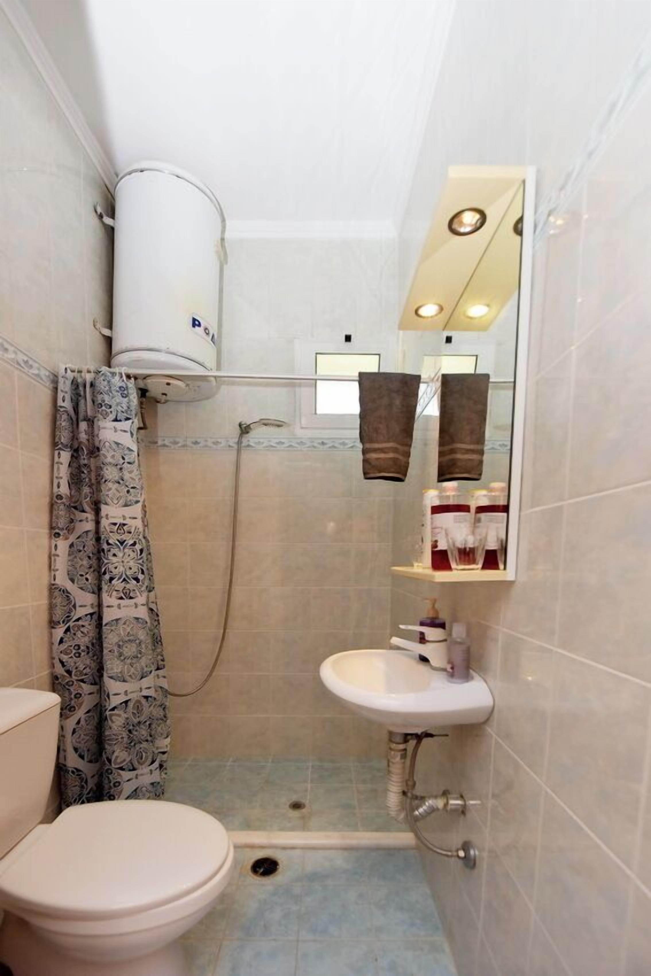 A small bathroom with a toilet, a shower, a sink, and a mirror.