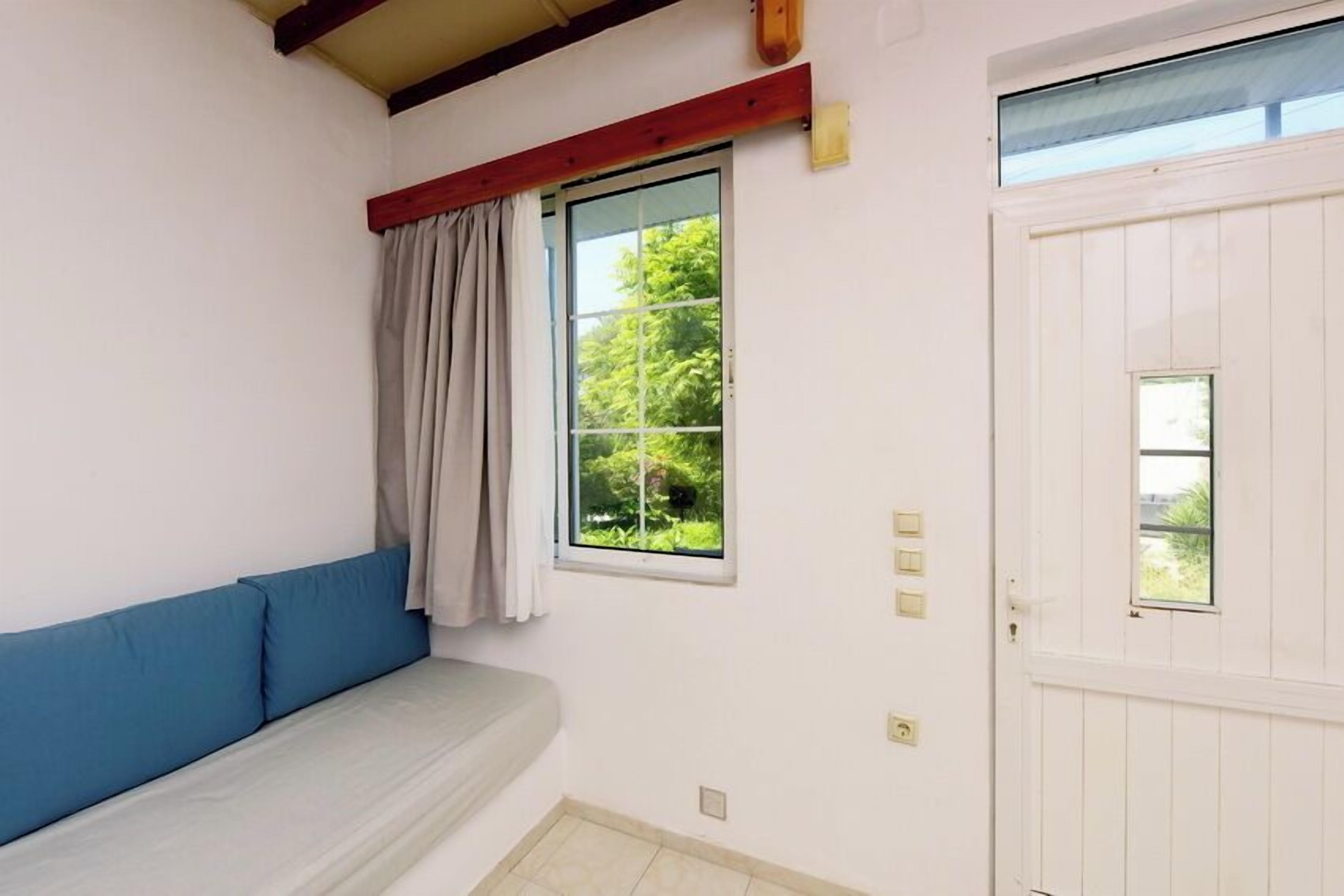 Ein Zimmer mit einer weißen Tür, einem Fenster mit Blick ins Grüne und einem blauen Sofa.