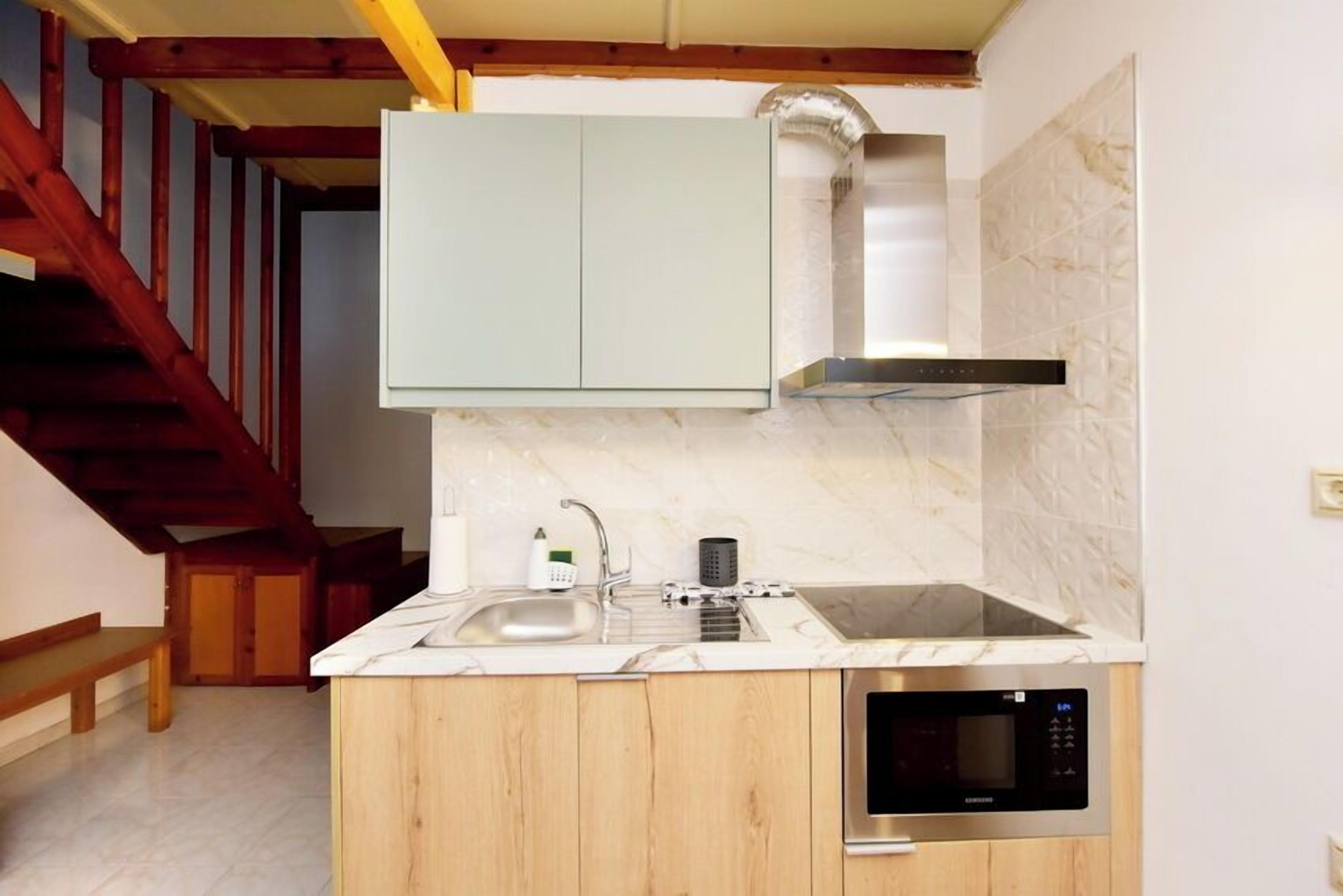 Una cocina compacta con microondas integrado, un lavamanos de acero inoxidable y armarios de madera.