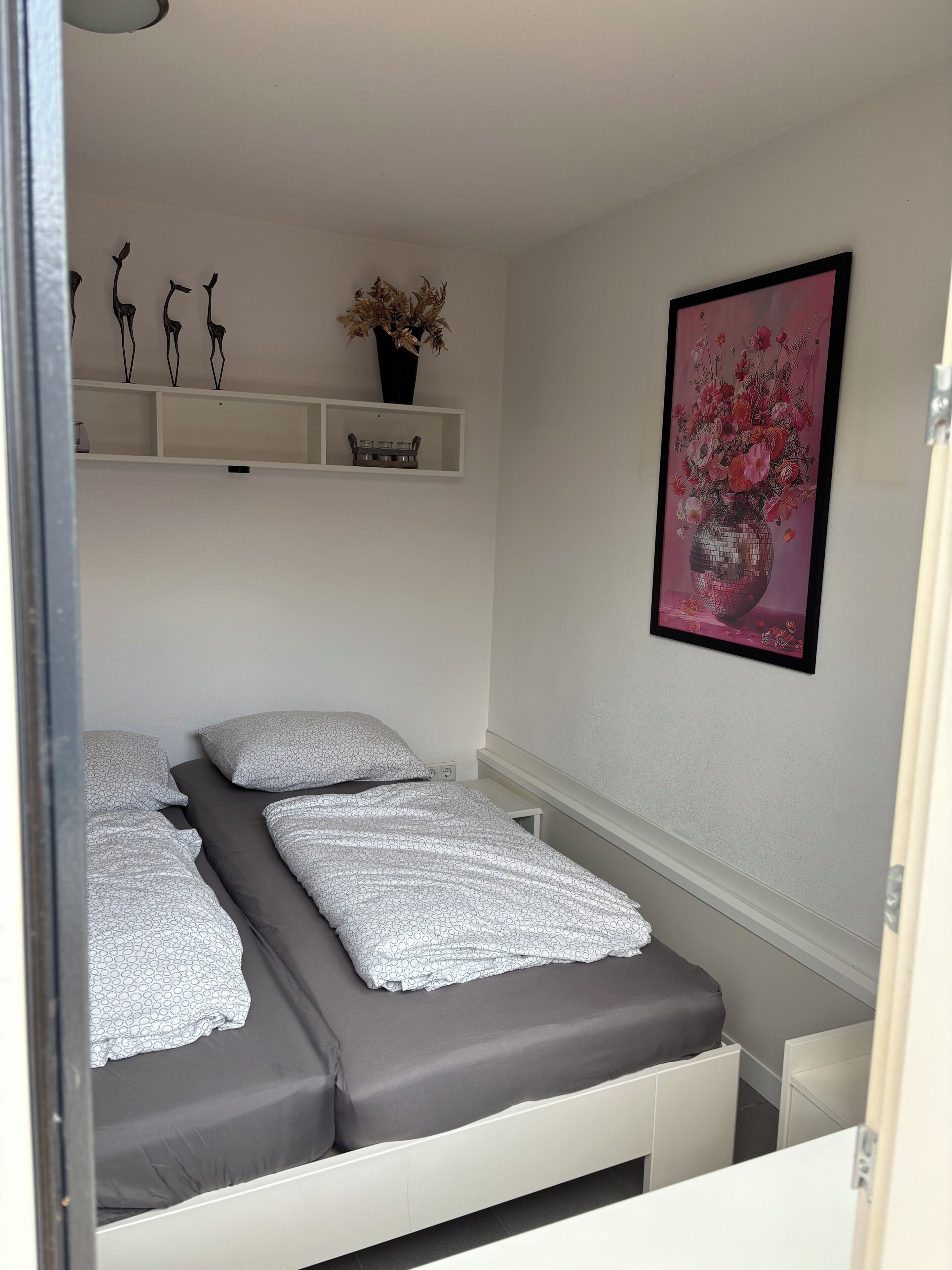 Un dormitorio con una cama, un estante con objetos decorativos y un cuadro en la pared.