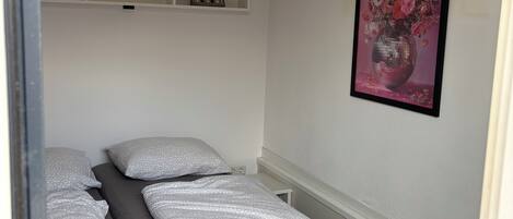 Un dormitorio con una cama, un estante con objetos decorativos y un cuadro en la pared.