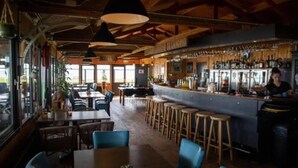 Un restaurante con zona de bar, techo de madera y taburetes de bar.