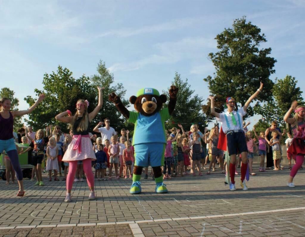 A group of people dancing outdoors with a mascot.
