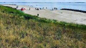 Una playa con tiendas de campaña, gente, zonas verdes y cielo despejado.