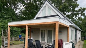 Un patio cubierto con una mesa y sillas, una estructura de pérgola de madera y un edificio residencial al fondo.