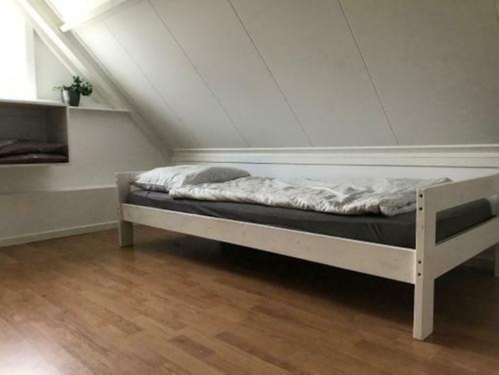 En säng för en person i ett rum med sluttande tak och trägolv.