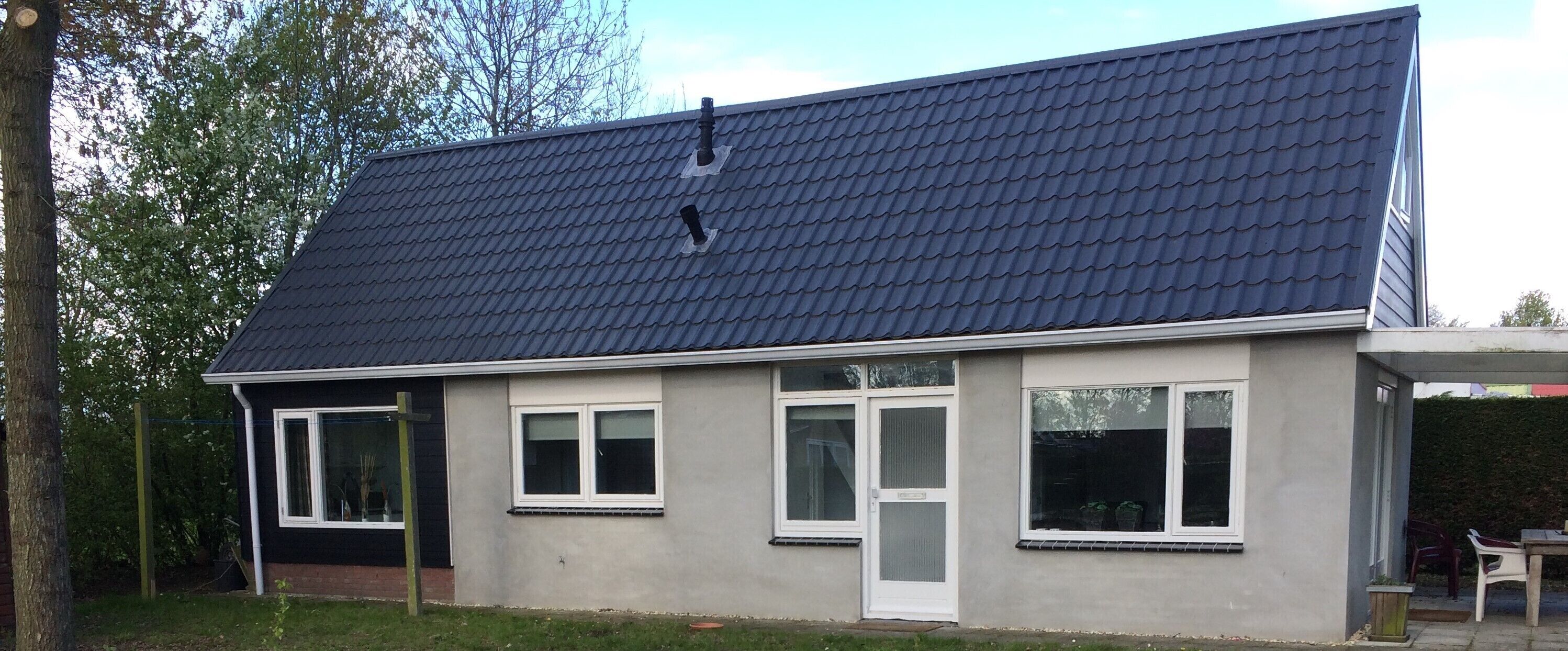 Een huis met twee verdiepingen, voorzien van een donker betegeld dak, witte kozijnen en een grijze gevel.