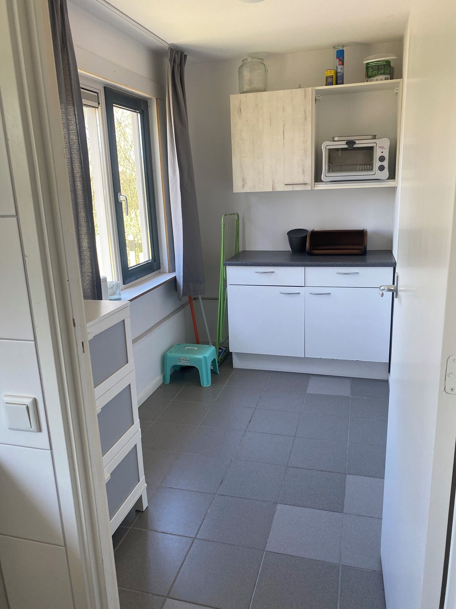 A compact kitchen with a microwave, a small refrigerator, and a window with curtains.