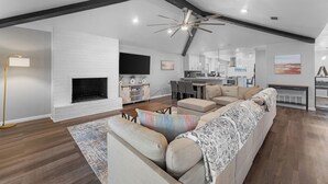 Amplia sala de estar con chimenea, un sofá grande, una mesa de comedor y una cocina al fondo.