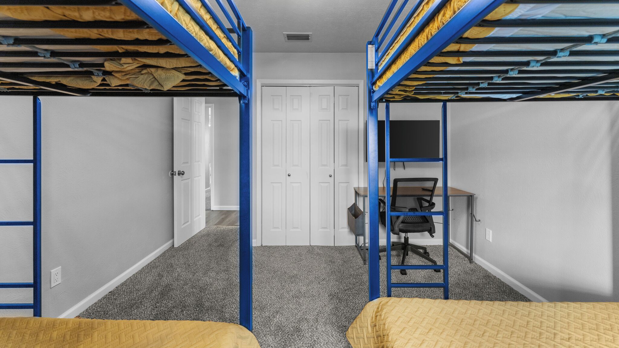 A dormitory room with bunk beds, a desk, and a chair.