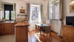 A kitchen with wooden cabinets, a dining table with chairs, a TV, and a window with curtains.