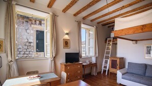 A cozy room with a wooden table, a sofa, a dresser, and a window with shutters.