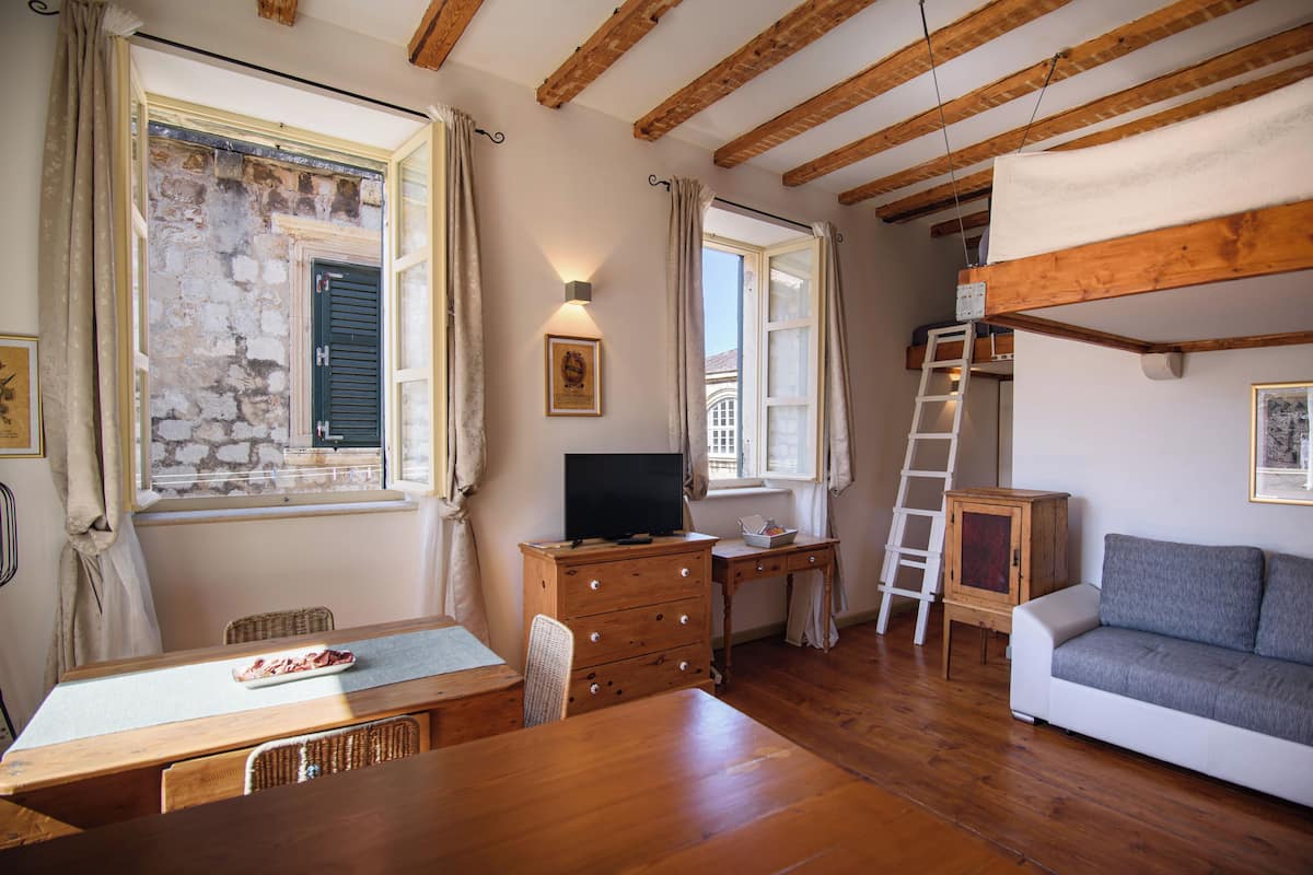 A cozy room with a wooden table, a sofa, a dresser, and a window with shutters.