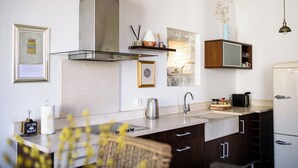 A modern kitchen with a stainless steel range hood, a built-in oven, a sink, and a refrigerator. There are decorative items on the wall and a wooden cabinet with drawers.