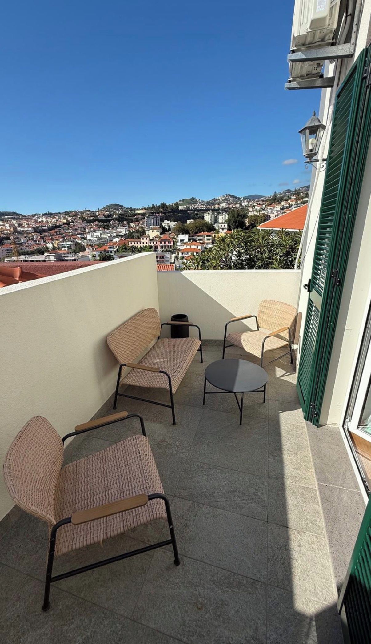 A balcony with wicker furniture, a small table, and a view of a town.