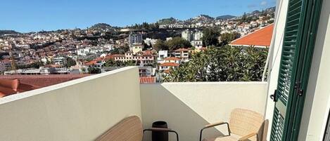 A balcony with wicker furniture, a small table, and a view of a town.