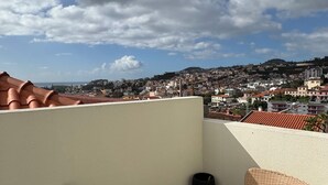 A terrace with wicker furniture and a view of a cityscape under a cloudy sky.