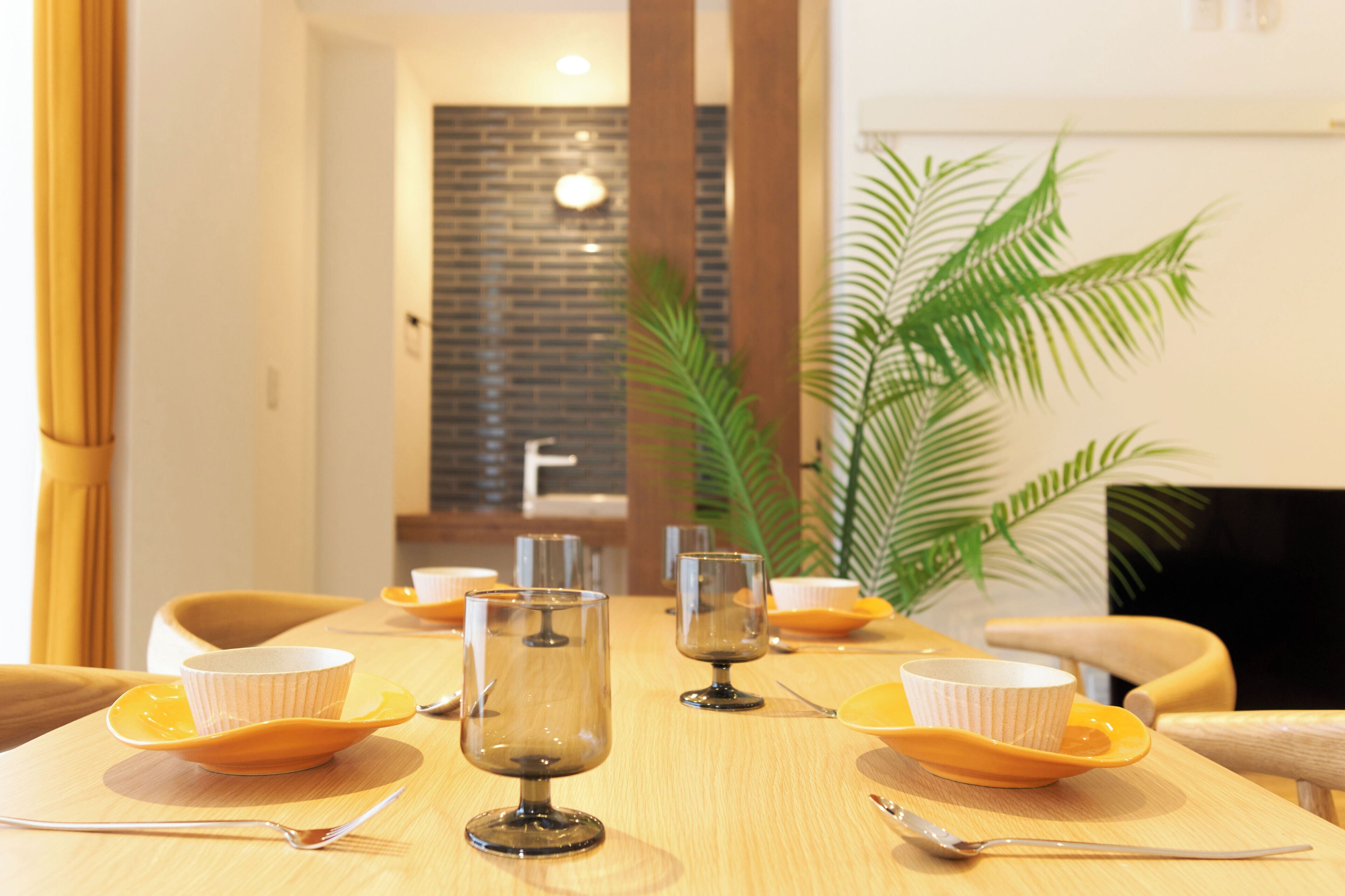 Una mesa de comedor con varias sillas, una planta y un muro de ladrillo al fondo.