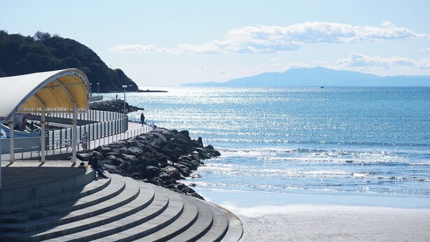 A coastal walkway with a curved stone design, a covered shelter, and a view of the sea and distant mountains. - Z LAND Enoshima by Tranova (Fujisawa)