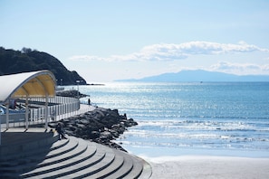A coastal walkway with a curved stone design, a covered shelter, and a view of the sea and distant mountains. - Z LAND Enoshima by Tranova (Fujisawa)