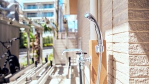 A shower area with a handheld showerhead and a wall-mounted faucet, a bicycle parked outside, and a building in the background. - Z LAND Enoshima by Tranova (Fujisawa)