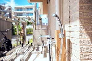 A shower area with a handheld showerhead and a wall-mounted faucet, a bicycle parked outside, and a building in the background.