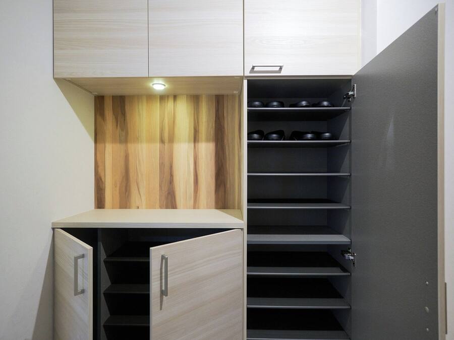A compact storage unit with a wooden finish, a built-in shoe rack, and a small illuminated shelf.