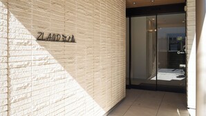 A building entrance with a brick wall and a glass door. - Z LAND Enoshima by Tranova (Fujisawa)