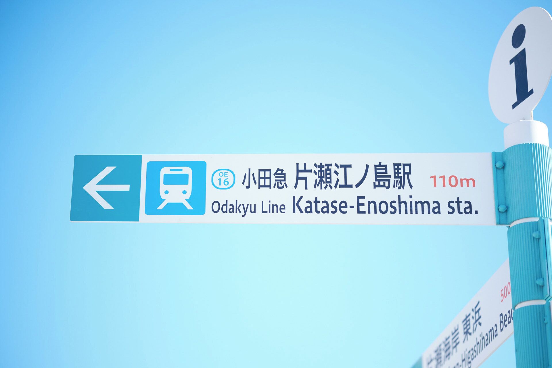 A directional sign for the Odakyu Line Katase-Enoshima station, indicating the station's name and distance.