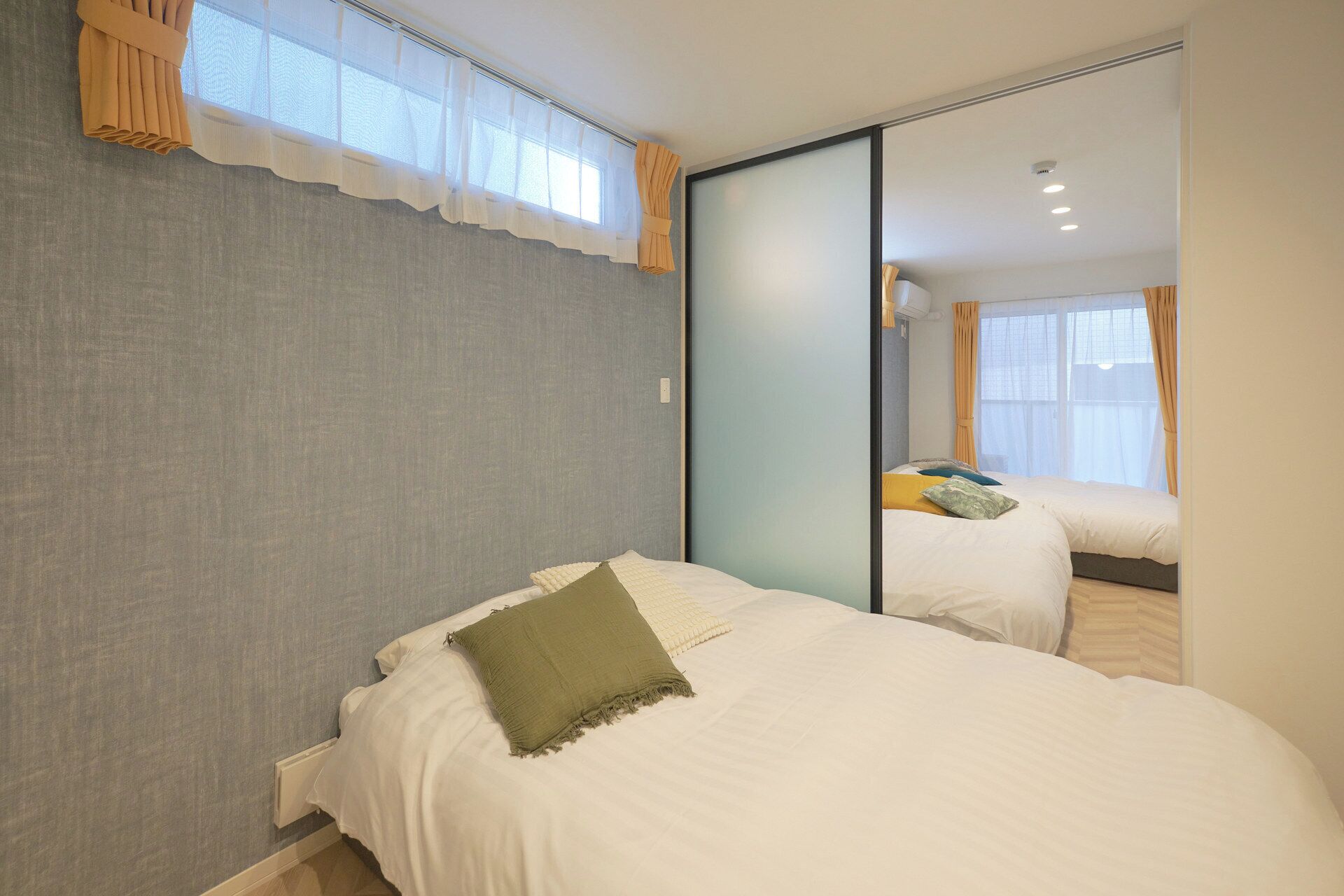 A bedroom with a large mirror, a bed with white bedding, and a view of another room through the mirror.