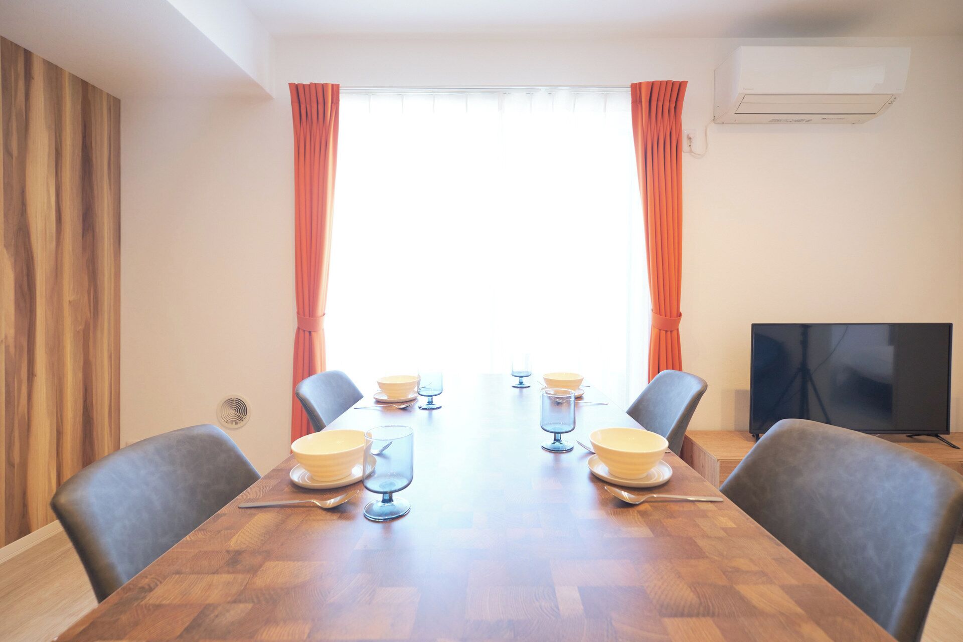 A dining area with a wooden table, four chairs, and a television on the wall.