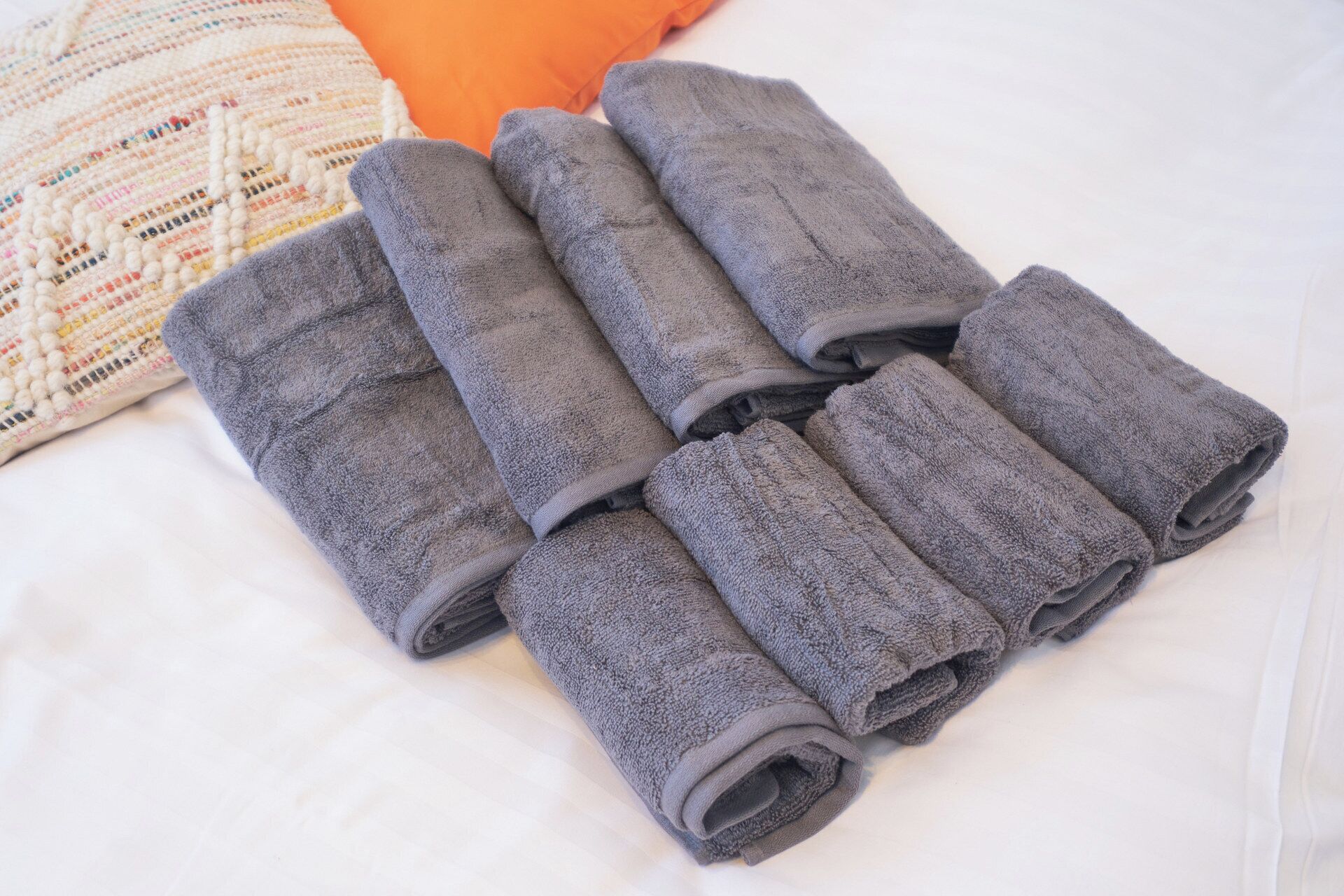 A bed with rolled gray towels and a patterned pillow.