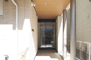 A narrow corridor with a glass door leading to a room, a metal fence on the right, and a wooden ceiling. - Z LAND Enoshima by Tranova (Fujisawa)