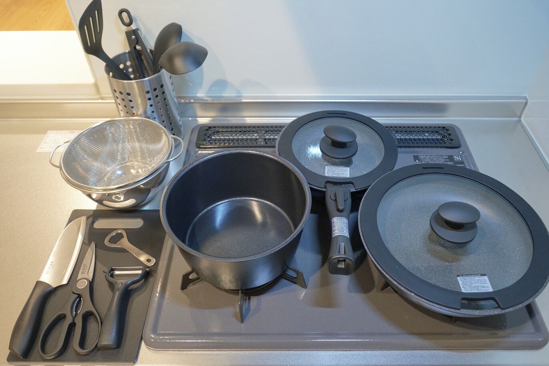 A kitchen counter with a strainer, a pot, a frying pan, a spatula, and a pair of scissors.