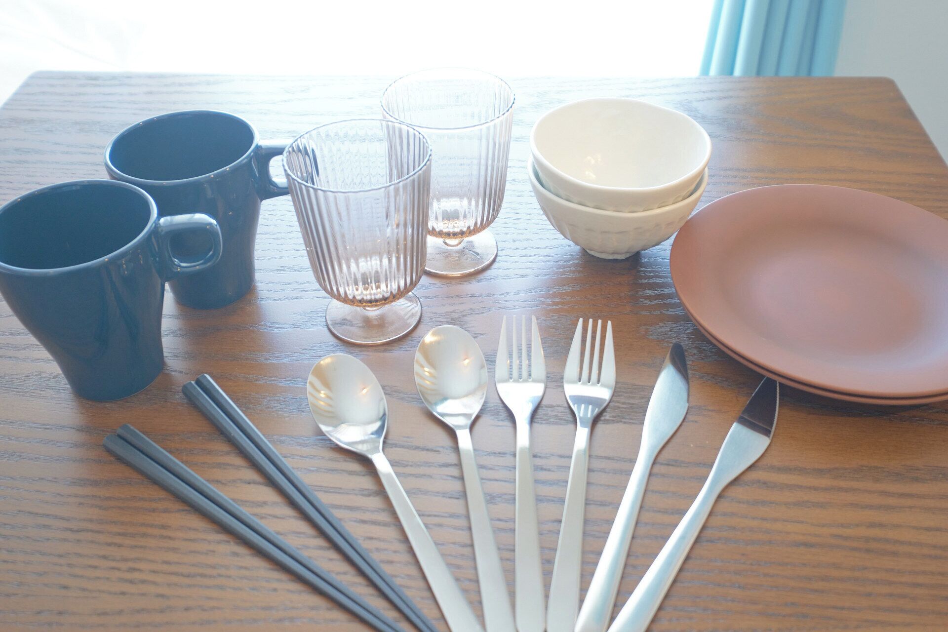 A table with a set of utensils, two cups, two glasses, and a bowl.