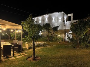 A well-lit outdoor area with a dining setup, a covered seating area, and a building in the background.