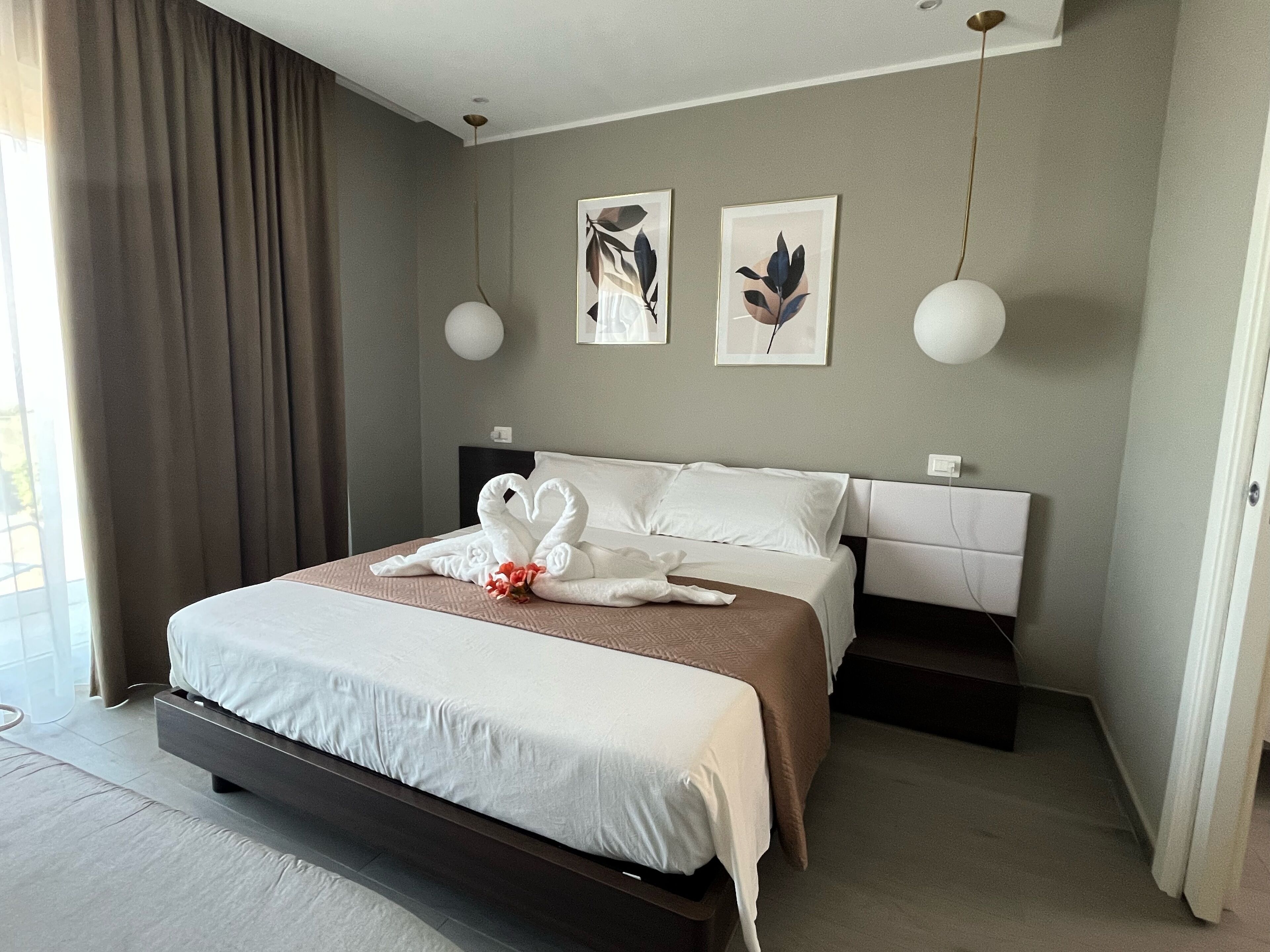 Quarto de hotel moderno com uma cama grande, uma mesa de cabeceira e duas luminárias fixadas na parede.
