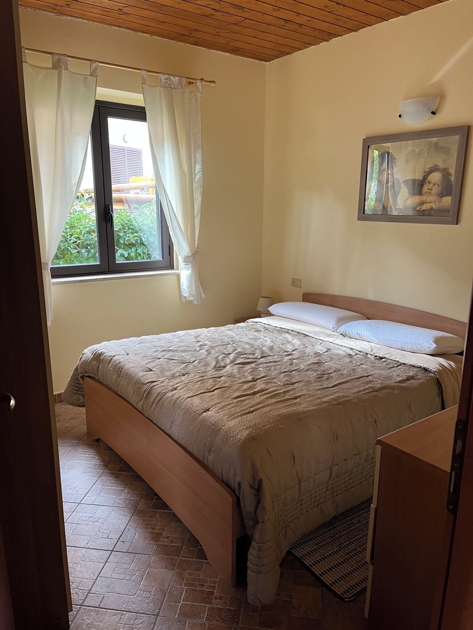 Ein Schlafzimmer mit Bett, einem Vorhangfenster, einem Bild an der Wand und einer Holzbalkendecke.