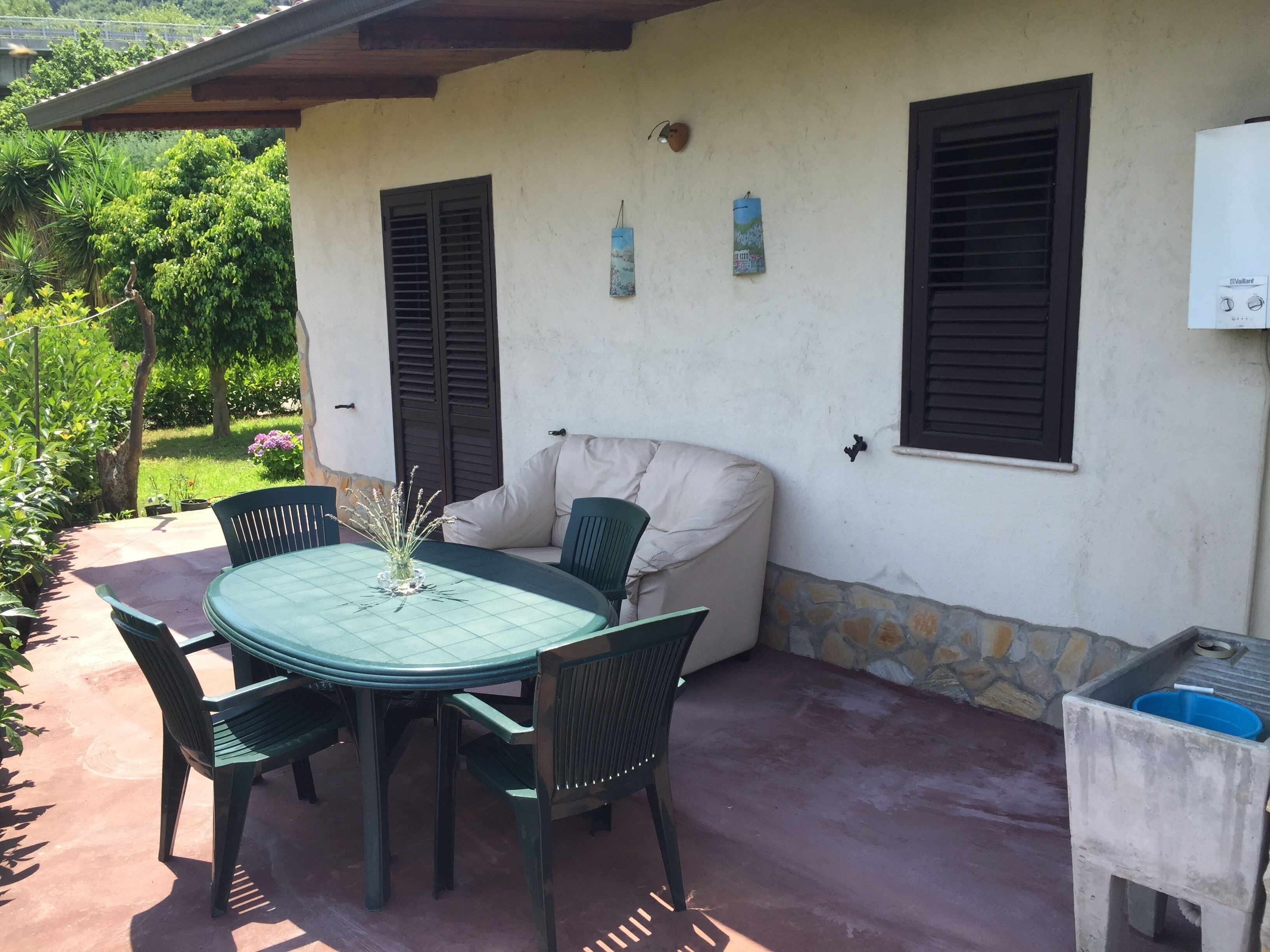 Une terrasse extérieure avec une table ronde et des chaises, un canapé beige et un mur en pierre.