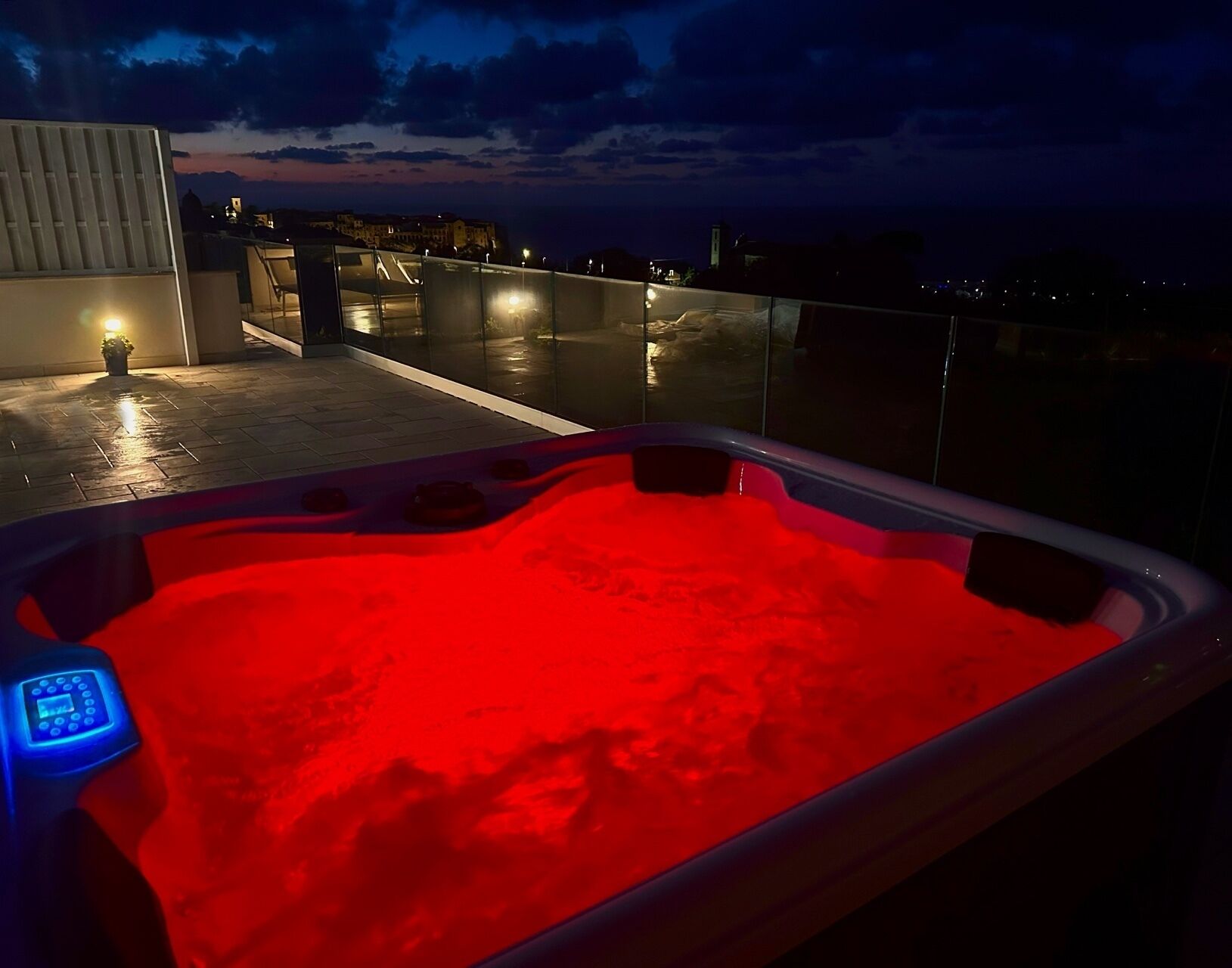 A hot tub with a red light on a rooftop terrace with a city view at dusk.